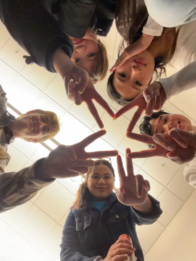 Five students leaning into a playful group photo taken from below.